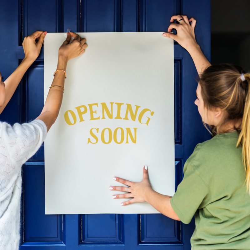Women putting on store opening soon sign